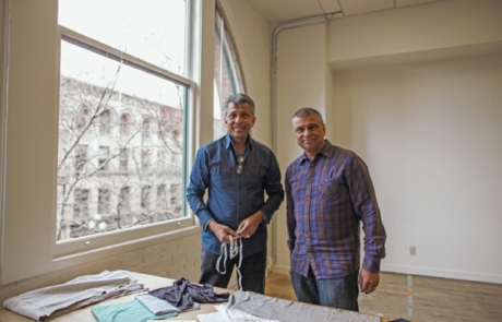The image depicts the two founders of the company, Raj and Akhil Shah. They are standing over a table and smiling.
